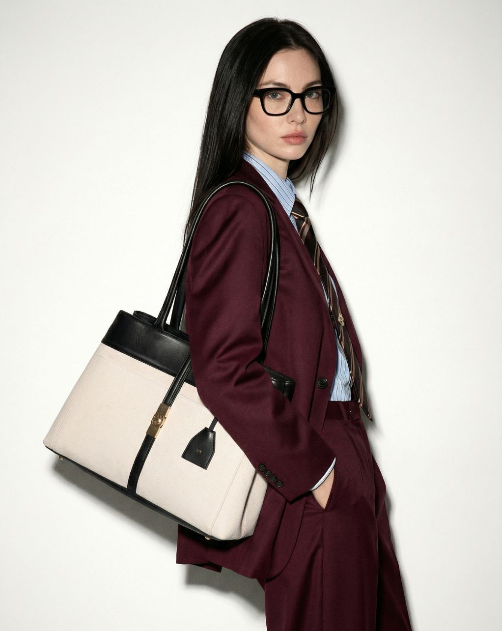 Woman in a burgundy suit holding a beige and black mindy tote